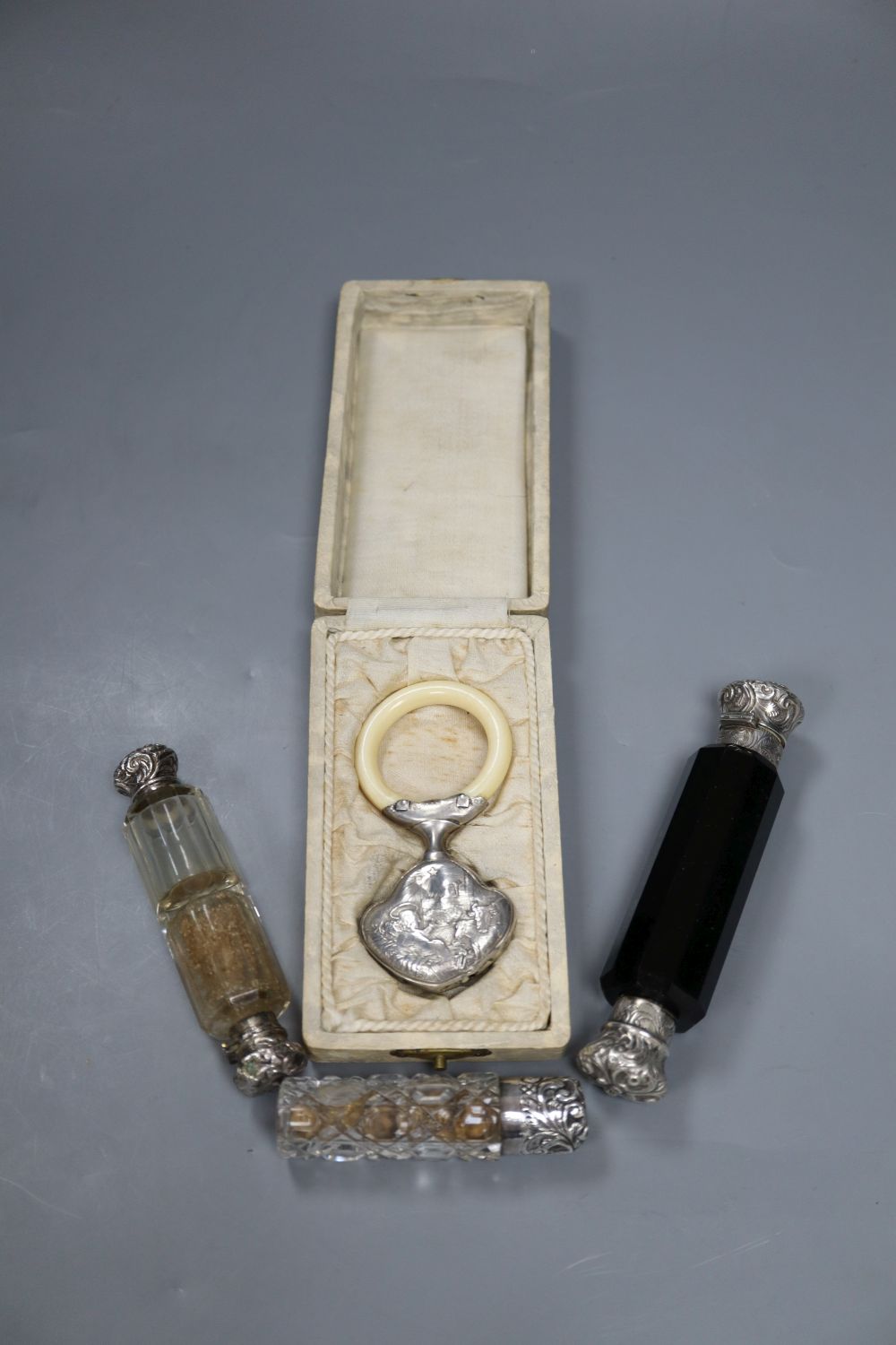 Three assorted white metal topped glass scent bottles including one silver and a childs white metal and ivory teether.